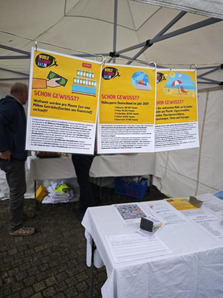 Drei gelbe Infoplakate mit der Überschrift „Schon gewusst?“ zu Plastikmüll in einem weißen Pavillon, davor ein Tisch mit Infomaterial