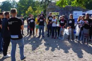 Helfer in World-Cleanup-Day-Shirts stehen im Halbkreis mit Säcken, im Vordergrund ein Mann von hinten, der die Gruppe begrüßt.