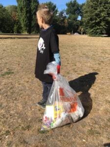 Ein Junge im World-Cleanup-Day-Shirt steht von hinten auf einer trockenen Wiese und hält einen prall gefüllten Sack.