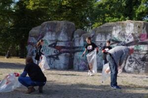 Mehrere Helfer sammeln mit durchsichtigen Säcken Müll am Fuß großer, mit Graffiti besprühter Felsen.