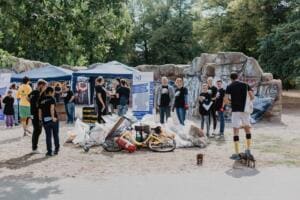 Auf einem Platz vor Pavillons und Graffiti-Felsen liegen gesammelte Säcke, Fahrräder und ein Feuerlöscher, ringsum Helfer und ein Hund.