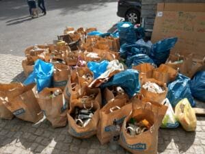 Viele volle Papier- und blaue Plastiksäcke stehen auf Pflaster vor einem handgeschriebenen Pappschild, das den Fleißigen im Treptower Park dankt.