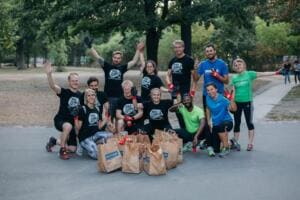 Ein gut gelauntes Team in Sportkleidung und World-Cleanup-Day-Shirts jubelt auf einem Parkweg hinter vollen Papiertüten.