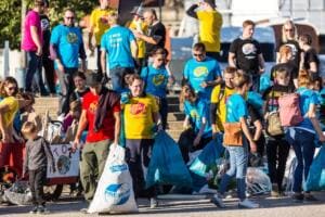 Eine große Gruppe in bunten Shirts steht mit vollen blauen und weißen Säcken an einer Treppe, darunter ein Kind.