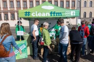 Unter einem grünen Pavillon mit der Aufschrift „#cleanffm“ melden sich viele Menschen an und holen Material ab.