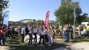 Eine große Menschenmenge versammelt sich auf einer Wiese am Mainufer zwischen zwei World-Cleanup-Day-Beachflags, im Hintergrund eine Eisenbahnbrücke.