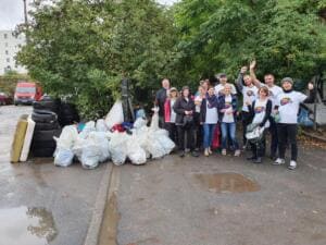Eine jubelnde Gruppe in World-Cleanup-Day-Shirts steht neben einem Berg aus weißen Säcken, alten Reifen und Matratzen auf einem Hof.