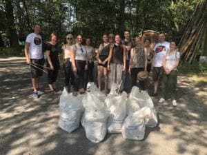 Eine Gruppe junger Erwachsener in Sommerkleidung steht im Wald hinter mehreren gefüllten weißen Säcken.