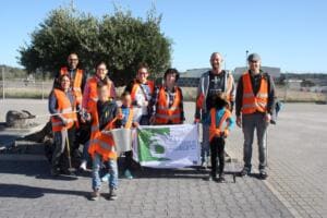 Eine Gruppe aus Erwachsenen und Kindern in orangefarbenen Warnwesten steht auf einem Parkplatz und hält eine Fahne mit der Aufschrift „Clean up Europe“.