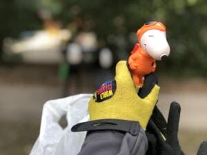 Eine Hand im gelben World-Cleanup-Day-Handschuh hält eine kleine orange-weiße Spielzeugfigur, die beim Sammeln gefunden wurde.