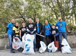 Eine Gruppe in blauen und schwarzen World-Cleanup-Day-Shirts, darunter ein Junge, steht mit vollen weißen Säcken an einer Brückenmauer.
