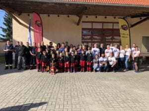 Eine große Gruppe aus Erwachsenen und Kindern in Feuerwehruniformen und World-Cleanup-Day-Shirts steht vor einem Gebäude mit zwei Beachflags.