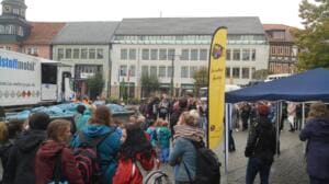 Viele Menschen, darunter Schulklassen, versammeln sich auf dem Marktplatz vor Pavillons, einer Beachflag und einem Lkw mit Müllsäcken.