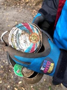 Nahaufnahme einer Hand in World-Cleanup-Day-Handschuh, die mehrere alte, verrostete Konservendosen hält.