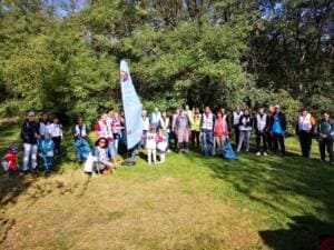 Eine große Gruppe aus Erwachsenen und Kindern, viele in World-Cleanup-Day-Westen, steht im Halbkreis auf einer Wiese am Waldrand um eine Beachflag.
