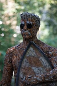 Nahaufnahme des Kopfes einer Skulptur aus tausenden Zigarettenstummeln mit Sonnenbrille, die ein Surfbrett hält.