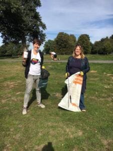 Zwei Frauen mit Müllsäcken stehen auf einer Wiese, eine davon im World-Cleanup-Day-Shirt.