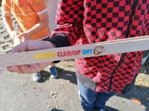 Nahaufnahme einer Kinderhand, die eine Holzgreifzange mit eingebranntem World-Cleanup-Day-Schriftzug hält.