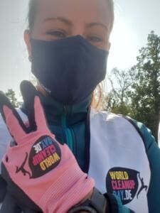 Selfie einer Frau mit Maske, die in einem pinken World-Cleanup-Day-Handschuh das Victory-Zeichen zeigt und eine World-Cleanup-Day-Weste trägt.