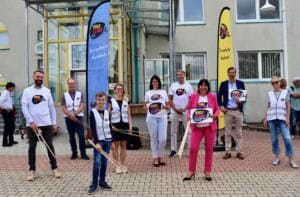 Eine Gruppe Erwachsener und ein Junge in World-Cleanup-Day-Shirts und Westen stehen mit Greifzangen vor einem Gebäude, daneben zwei Beachflags.