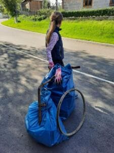 Ein Mädchen steht von hinten an einer Straße neben zwei vollen blauen Säcken und einem alten Metallring.