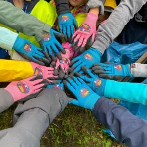 Von oben fotografiert strecken viele Kinderhände in bunten World-Cleanup-Day-Handschuhen sich in einem Kreis zusammen.