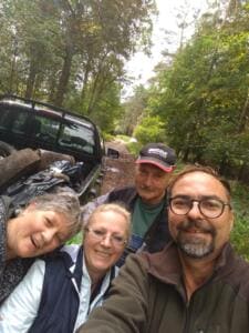 Vier lachende Erwachsene machen ein Selfie vor einem Pick-up, dessen Ladefläche mit vollen Säcken und Sperrmüll beladen ist.