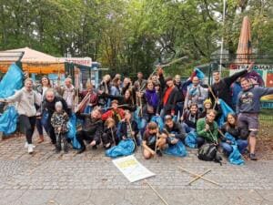 Eine große Gruppe reckt vor dem Eingang des Strandbads Plötzensee jubelnd Greifzangen und blaue Müllsäcke in die Höhe.