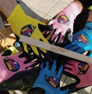 Mehrere Hände in bunten World-Cleanup-Day-Handschuhen liegen übereinander auf einem Holzstab mit eingebranntem Logo der Wirtschaftsjunioren.