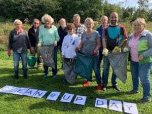 Zehn Erwachsene stehen mit Müllsäcken auf einer Wiese, vor ihnen liegen Papierbögen mit den Buchstaben Clean Up Day.
