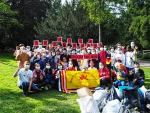 Eine große Gruppe mit Masken hält rote Schilder mit Buchstaben und ein Banner der Buddha's Light International Association, vor ihnen liegen volle Müllsäcke im Park.