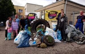 Eine Gruppe aus Erwachsenen und Kindern steht vor World-Cleanup-Day-Bannern hinter einem großen Traktorreifen, Säcken, Draht und anderen Fundstücken.