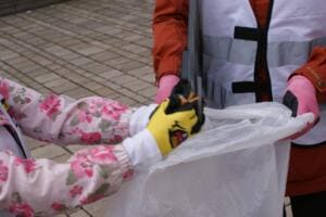 Nahaufnahme von Kinderhänden in Handschuhen, die gesammelten Müll in einen durchsichtigen Beutel werfen.