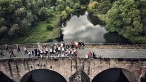Luftaufnahme einer großen Gruppe in Warnwesten auf einer alten Steinbogenbrücke über die Werra.