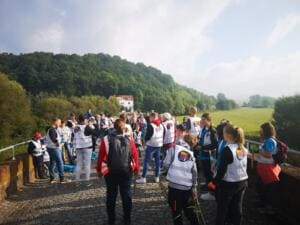 Viele Menschen in World-Cleanup-Day-Westen versammeln sich auf einer gepflasterten Brücke, im Hintergrund bewaldete Hügel.