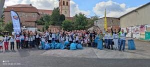 Eine große Gruppe in Warnwesten jubelt vor einem historischen Gebäude, vor ihnen liegen viele volle blaue Müllsäcke.