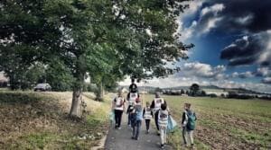 Eine Gruppe in Warnwesten geht mit Müllsäcken einen Weg entlang zwischen Bäumen und Feldern.