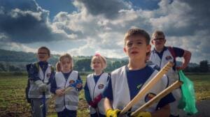 Fünf Kinder in World-Cleanup-Day-Westen stehen mit Holzgreifzangen vor einem Feld unter dramatischem Wolkenhimmel.