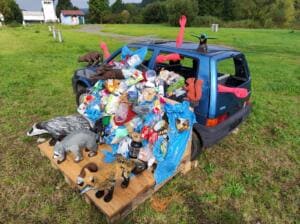 Nahaufnahme eines alten Autos, das mit Plastikflaschen, Verpackungen und Tierfiguren wie Dachs, Fuchs und Eichhörnchen dekoriert ist.