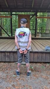 Ein Mann in World-Cleanup-Day-Warnweste steht von hinten vor einer hölzernen Bühne im Wald.