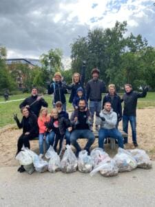 Eine Gruppe Erwachsener und Kinder sitzt und steht in einem Park um eine Bank, davor liegen viele durchsichtige Säcke mit gesammeltem Müll.