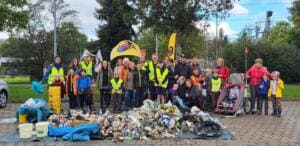 Eine große Gruppe aus Kindern und Erwachsenen steht hinter einem großen Haufen gesammelten Mülls auf einer Plane, im Hintergrund World-Cleanup-Day-Beachflags.