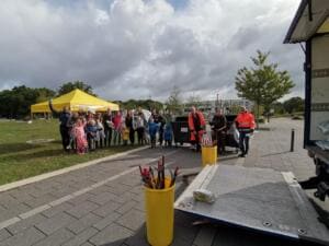 Eine Gruppe aus Familien und Beschäftigten der Abfallwirtschaft steht neben einem gelben Pavillon und Müllcontainern, im Vordergrund ein Eimer mit Greifzangen und die Ladefläche eines Lkw.