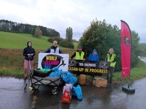 Fünf Personen stehen hinter Bannern von World Cleanup Day und Sea Shepherd, davor ein Bollerwagen mit Reifen, Säcken und Kanistern.
