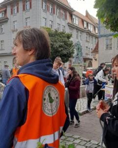 Ein Mann in orangefarbener Weste mit dem Aufdruck Sauberes Aschersleben steht in der Altstadt, im Hintergrund viele Kinder und Erwachsene an einem Stand.