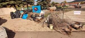 Auf einem gepflasterten Platz liegen sortierte Haufen aus Müllsäcken, Reifen, Holz, Draht und Metallschrott, an einem Zaun hängt ein World-Cleanup-Day-Banner.