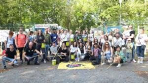 Eine große Gruppe mit Greifzangen und grünen Eimern steht und kniet vor dem Eingang des Freibads Plötzensee, vorne liegt ein World-Cleanup-Day-Banner.