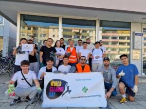 Eine Gruppe junger Männer und Frauen kniet und steht vor einem Gebäude mit einem Banner, auf dem World Cleanup Day und Focus Humanitarian Assistance steht.