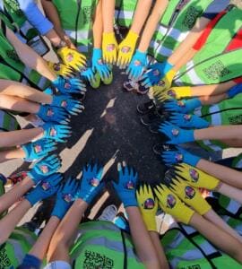 Von oben fotografiert strecken viele Kinder in grünen Warnwesten ihre Hände in bunten World-Cleanup-Day-Handschuhen in einem Kreis zusammen.