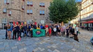Eine große Gruppe aus Erwachsenen und Kindern mit Paddeln, Greifzangen und einem grünen World-Cleanup-Day-Banner steht auf dem Marktplatz vor dem Rathaus, vorne sitzt ein brauner Hund.